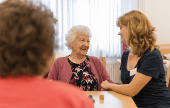 Betreuerin und ältere Dame lachend am Tisch sitzend