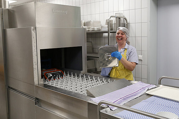 Mitarbeiterin in der Großküche beim Entladen der Spülmaschine